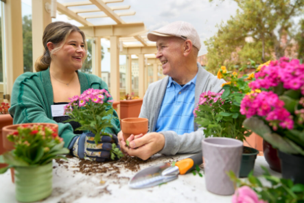Resident and team member sharing conversation while potting flowers together during gardening activity in community’s outdoor courtyard